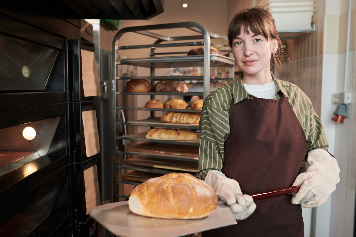 Portrait of baker looking at camera while taking fresh bread out of the oven